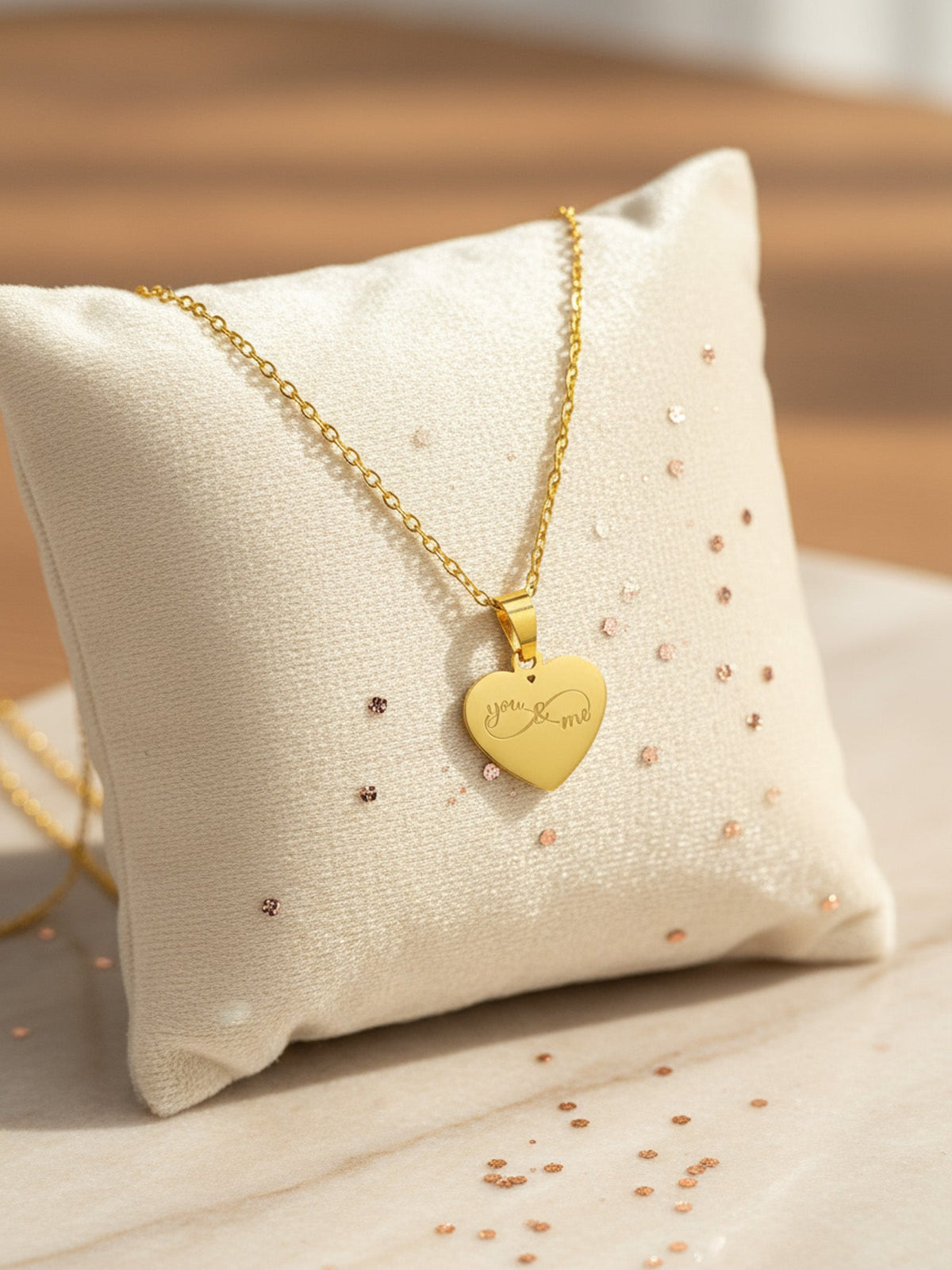 Goldfarbene Herzkette mit persönlicher Gravur auf einem hellen Kissen – eine Geschenkidee von MaJe Pictures
