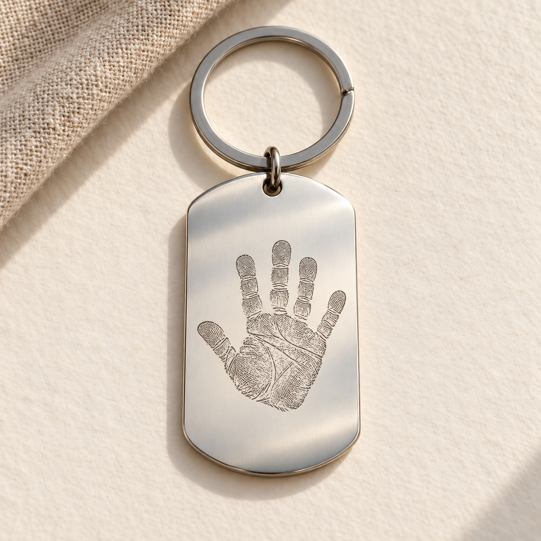 KI-Gestaltungsbeispiel: silberfarbener Edelstahl-Dogtag mit einer fiktiven Kinderhand als feine Line-Art-Gravur und Schlüsselring; kein Kunden- oder Musterfoto.