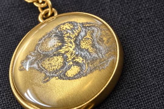 Makroansicht der Glaskuppel über der Pfotengravur beim goldfarbenen Armband.